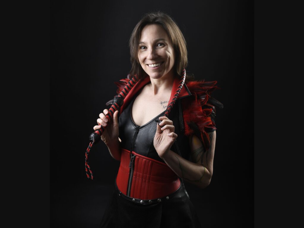 Portrait von Jay in Federn mit Peitsche, bereit für die BDSM-Studio Führung