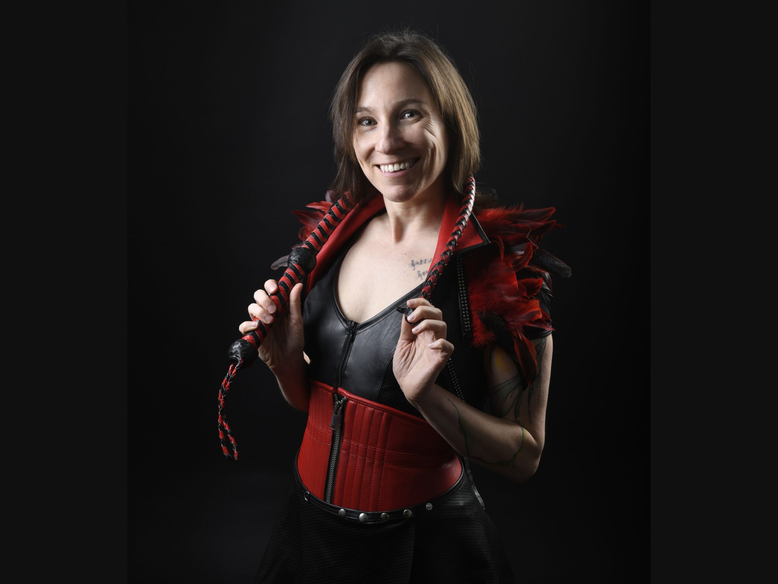 Portrait von Jay in Federn mit Peitsche, bereit für die BDSM-Studio Führung