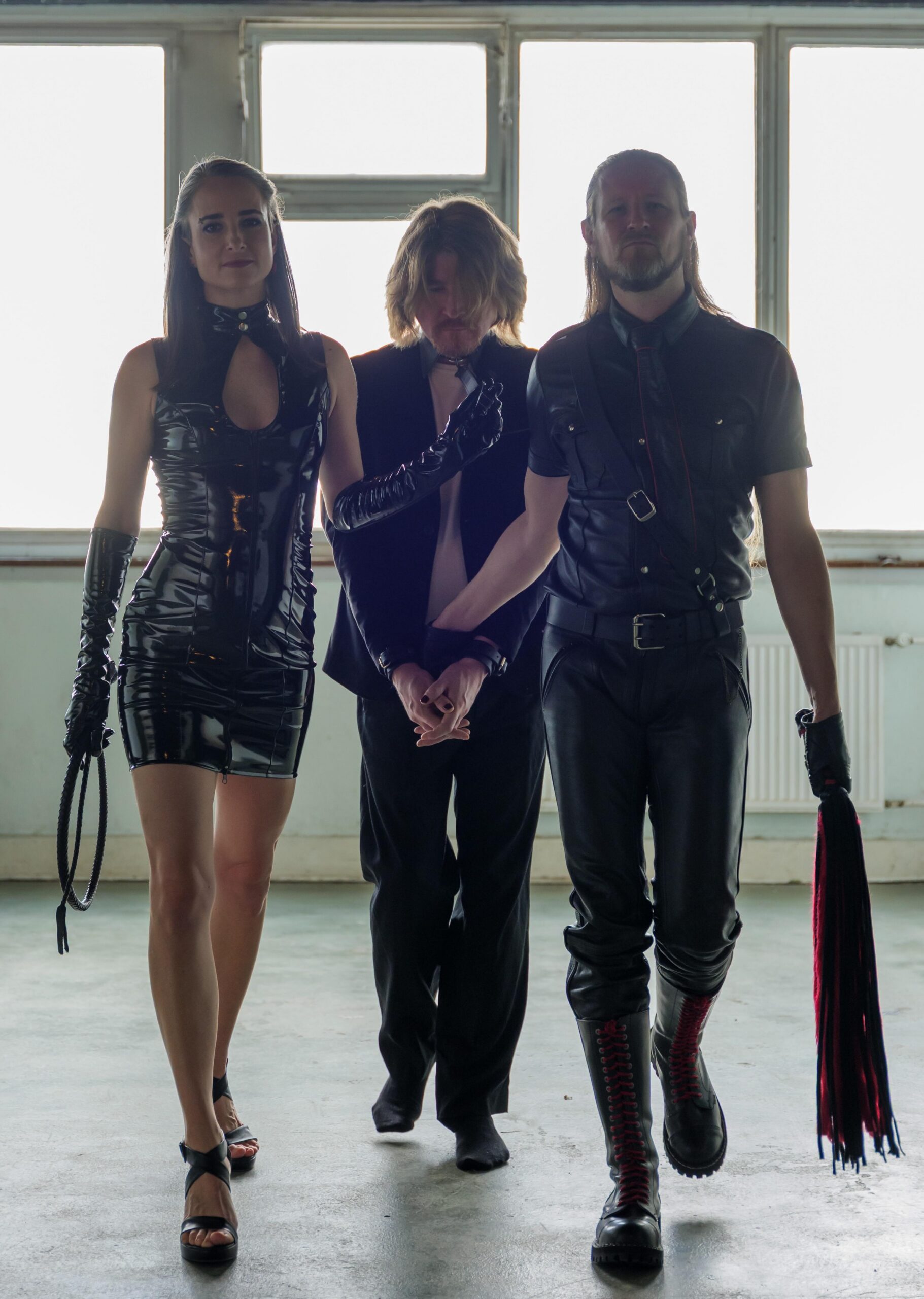 Hekate 12 mit Samael Foto von Hekate, einer großen, schlanken Domina, einem Sub am Halsband in der Mitte, und rechts Master Samael, ein großer Dom mit blonden langen Haaren und Flogger.
